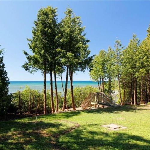 Private waterfront setting with a spacious grassy yard, mature trees, and direct access to the clear waters of Lake Huron.