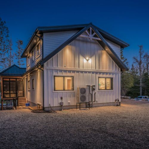 Modern cabin-style vacation rental tucked in the woods, featuring warm exterior lighting, screened porch, and ample parking—perfect for nature escapes, lakeside retreats, or weekend getaways.