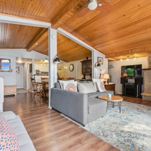Warm and inviting open-concept living space with wood-paneled vaulted ceilings, cozy seating, and charming cottage décor.