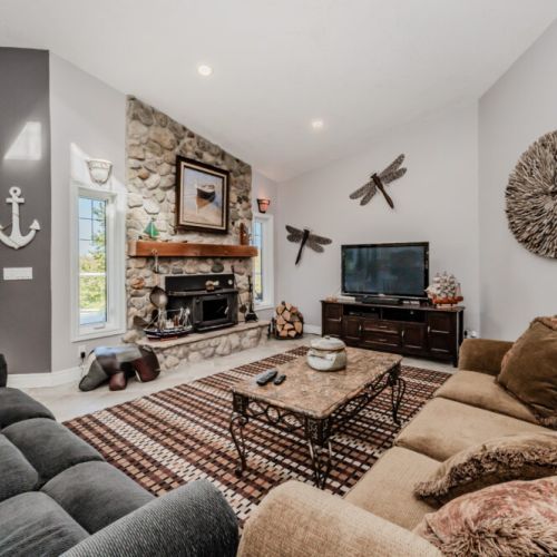 Unwind in a stylish living room featuring a stone fireplace, nautical decor, and forest views—perfect for a peaceful retreat or family movie nights at your vacation rental