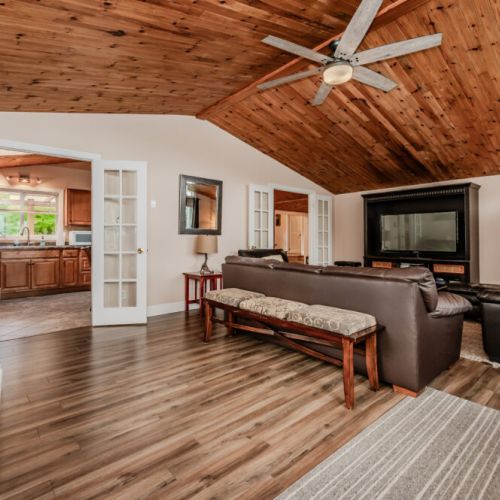 Spacious living area with vaulted wood ceilings, cozy seating, and French doors leading to a bright kitchen—ideal for relaxation and entertaining.