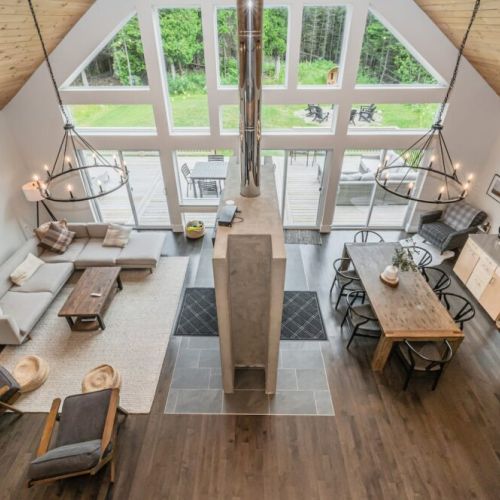 The stunning Great Room provides ample room for rest and relaxation. It features a large double-sided fireplace, dining table, games table, coffee bar, OLED TV, modern art, dramatic floor-to-ceiling windows and two exits to the back deck and lawn.