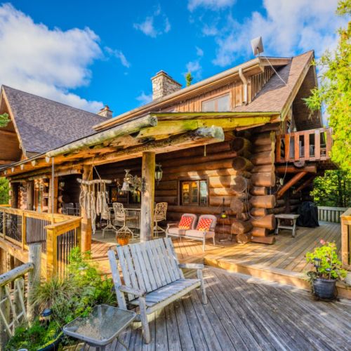 The stunning log cabin’s wraparound deck showcases the property’s natural beauty and offers ample seating areas, blending rustic charm with outdoor comfort.