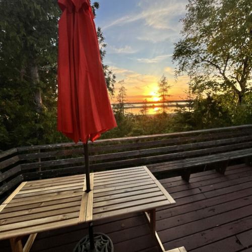 A cozy deck area with a red umbrella and wooden picnic tables, perfect for outdoor dining while enjoying the sunset and natural surroundings.