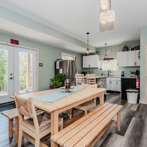 Enjoy family meals at this rustic dining table with direct deck access and a bright, modern kitchen just steps away—great for cottage entertaining.