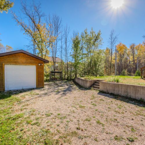 The property includes a detached garage and a large gravel driveway, providing ample parking for multiple vehicles. The surrounding greenery and nearby trees create a private and tranquil outdoor space, perfect for outdoor activities or simply enjoying nature.