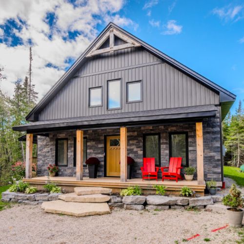 The front porch features cozy Adirondack chairs, inviting you to relax and take in the peaceful surroundings of this woodland escape.