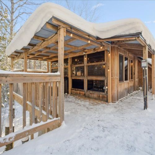 The covered entry and hot tub area framed by fresh snow and warm lighting. A cozy winter retreat you’ll look forward to every day.