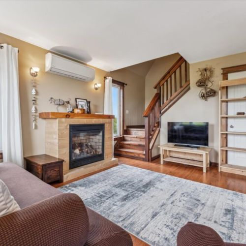 Warm and inviting sitting area with a gas fireplace, smart TV, and natural wood staircase leading to the upper level.