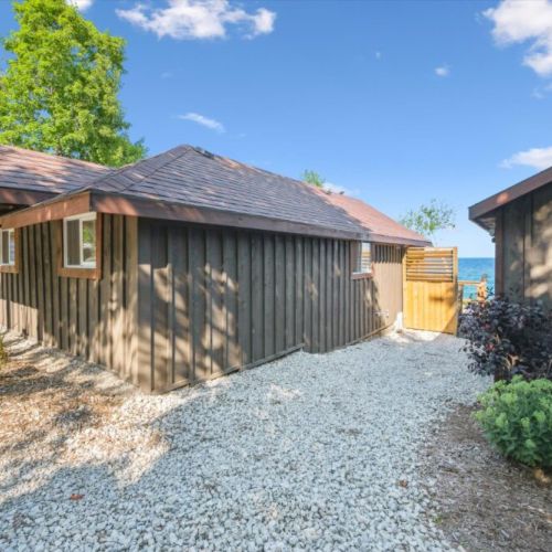 Charming gravel walkway leading toward the deck and shoreline. Rustic cedar siding meets water views for a true cottage feel.