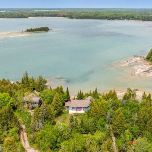 Perched in a quiet, wooded nook on the shoreline, the cottage sits perfectly tucked into its surroundings, just steps from the crystal-clear water.