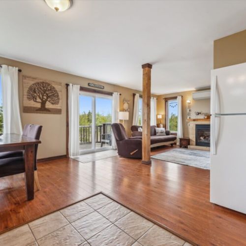 The spacious main floor features a seamless transition from dining to lounging, with a gas fireplace, full-glass patio doors, and warm wood flooring throughout.
