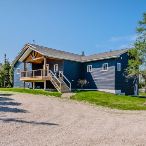 This wide shot captures the cottage amidst its serene surroundings. The expansive property, highlighted by the beautiful wooden porch and scenic backdrop, offers guests an idyllic escape into nature.