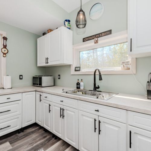 Cook with a view in this fully equipped kitchen featuring bright cabinetry, large windows, and all the comforts of home in a forested retreat.