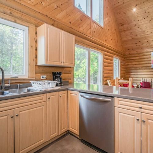 Clean up is a breeze with the dishwasher and double sink. The open-plan design of the kitchen extends into the living area, ideal for socializing while preparing meals, with a view of the natural wood interior that adds warmth to the space.
