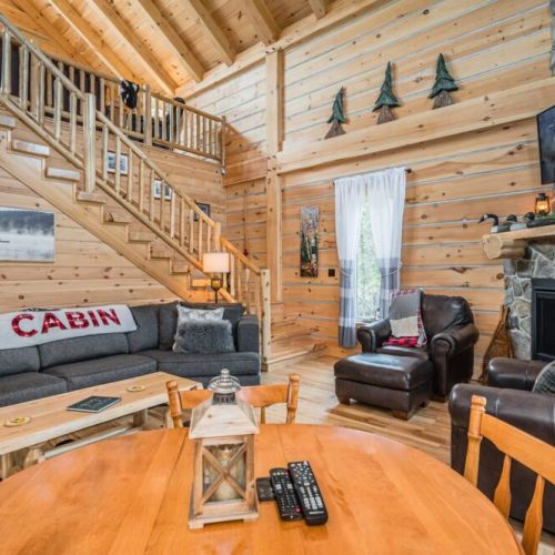 The grandeur extends into the cozy living area, featuring handcrafted log furniture and luxurious leather seating, perfect for gatherings around the majestic stone fireplace.