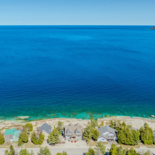 A perfect summer’s day at Lions Den Cottage: vibrant turquoise waters stretching endlessly into the horizon, framing the charming lakeside cottages below.