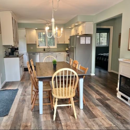 Gather with friends and family around this warm wooden dining table, lit by a cozy chandelier — a welcoming space for shared moments and laughter.