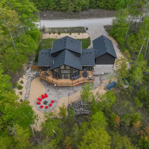 Discover the ultimate retreat with an aerial view of the house and its picturesque surroundings. The expansive deck and inviting fire pit area are nestled within lush greenery, providing a serene and private vacation haven.