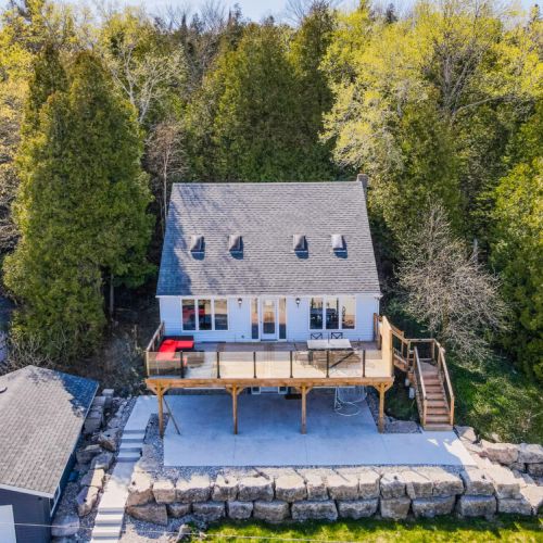 Picturesque front view of the charming cottage, set amidst lush greenery. The spacious deck, complete with comfortable seating, offers a stunning view of the lake, perfect for outdoor dining and relaxation.