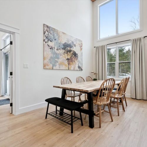 Open dining area with handcrafted table, bench seating, and tall windows filling the space with natural light.