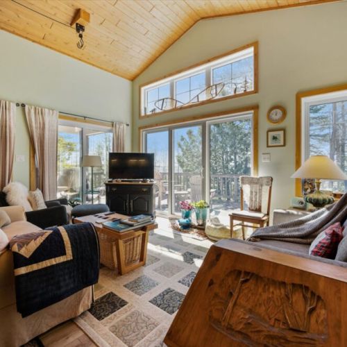 Large windows fill the living room with natural light while offering peaceful views of the surrounding trees and sparkling water.