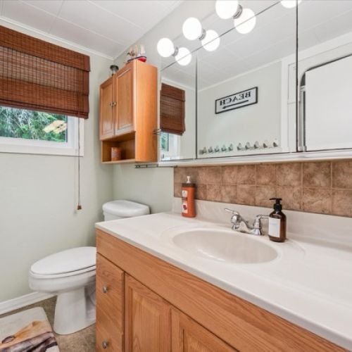 Bright and inviting bathroom featuring a large mirrored vanity, warm wood cabinetry, and ample natural light.