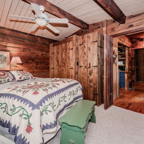 Step into comfort in this rustic bedroom, featuring a cozy quilted bed, natural wood finishes, and direct access to the heart of the home—perfect for relaxing forest getaways and weekend retreats.