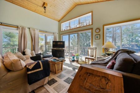 Large windows fill the living room with natural light while offering peaceful views of the surrounding trees and sparkling water.