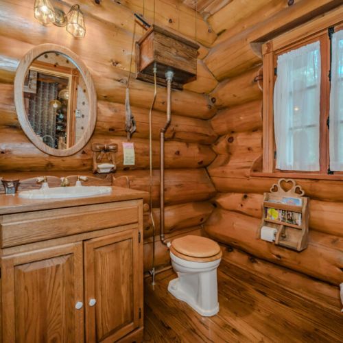 The bathroom exudes rustic elegance with its natural wood walls, unique log detailing, and a charming circular mirror, creating a cozy and functional space.