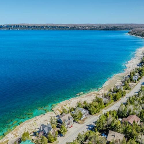 Coastal road hugging the shoreline with panoramic lake views and charming cottages—ideal for scenic drives, lakeside living, and photography lovers.