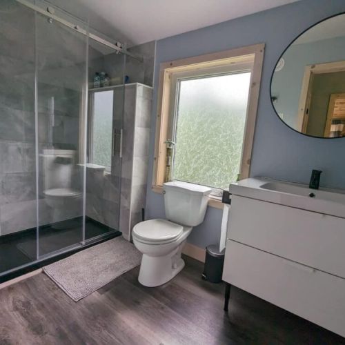 Modern upper-level bathroom with a walk-in glass shower, large vanity, and warm natural light—spa-like comfort in cottage style.