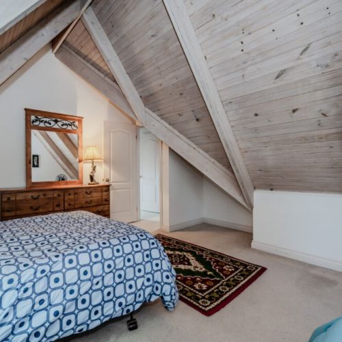 This charming attic bedroom features sloped ceilings and warm wooden accents, offering a cozy and inviting space to recharge. Perfect for those seeking a peaceful and rustic touch during their Georgian Bay getaway.
