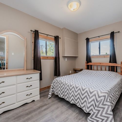 This second bedroom offers natural light, a comfortable bed, and a large dresser with mirror, perfect for a relaxing retreat.