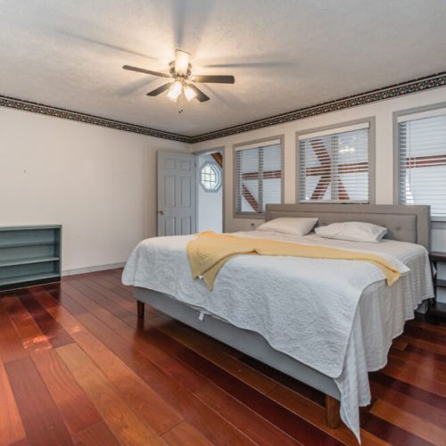 A spacious master bedroom featuring hardwood floors, a ceiling fan, and ample natural light.