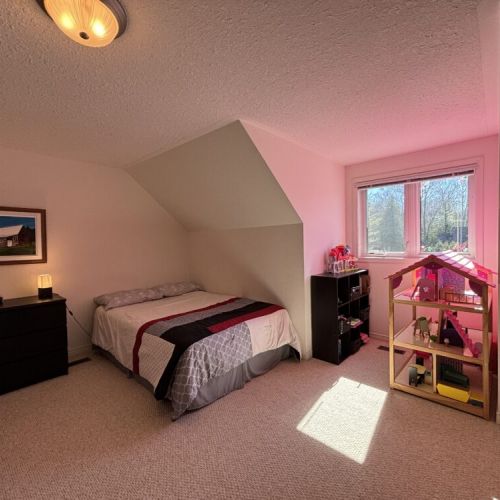 The guest bedroom has plenty of natural light, offering a cozy corner for dreams and play with a dollhouse and toys by the window, perfect for kids.