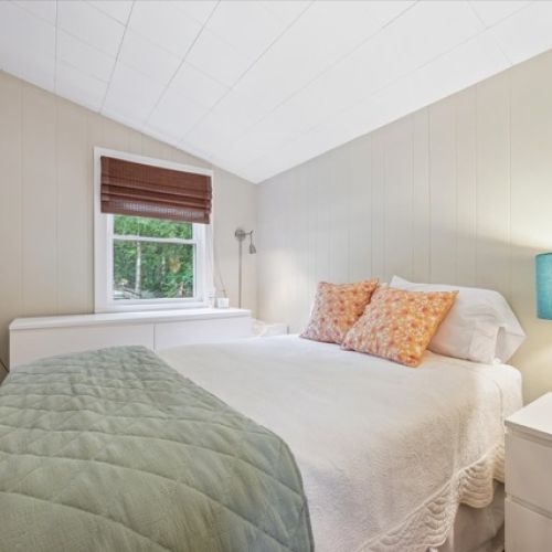 Bright and airy bedroom featuring a cozy bed, colourful accents, and soft natural light from the window.