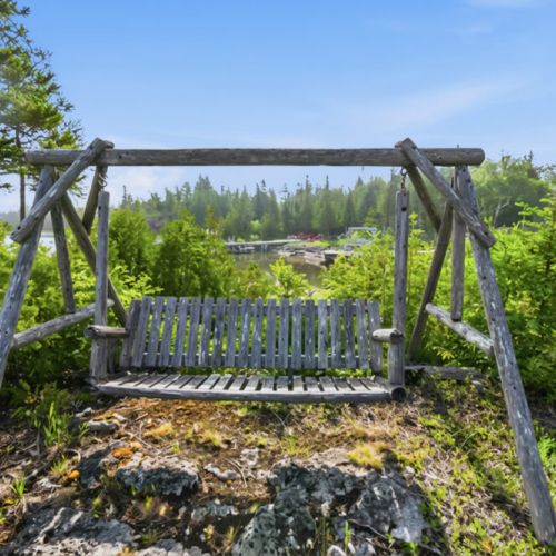 A rustic wooden swing overlooks the shoreline and surrounding forest. An ideal spot for slow travel, peaceful moments, and enjoying nature on your lakeside retreat.