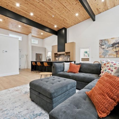 Inviting open-concept living area featuring a plush sectional, warm wood ceilings, and a stylish modern kitchen beyond.