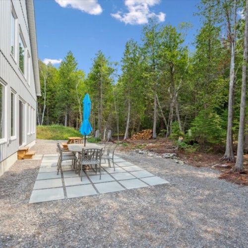 A stone patio with dining table and umbrella offers a lovely spot for alfresco meals and forest views.