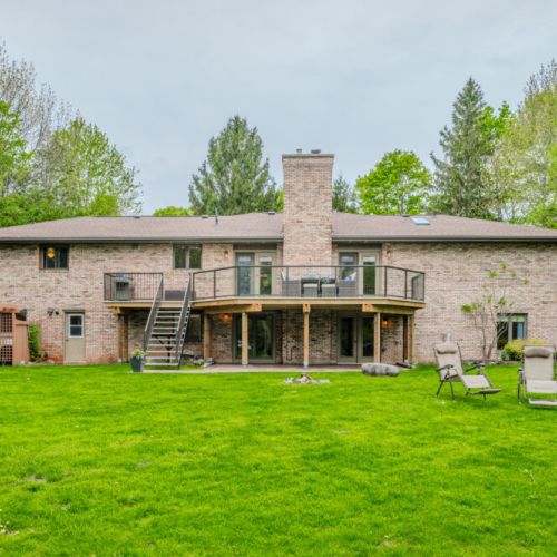 Picturesque rear view of the home with manicured lawn, deck seating, and natural surroundings—designed for restful outdoor living.