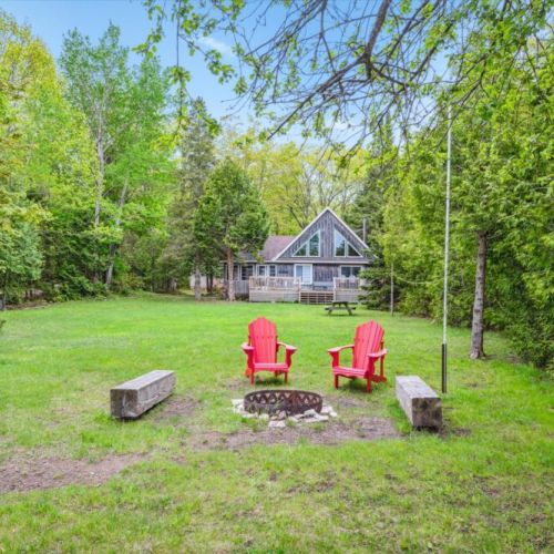 Looking back from the water, the lush open yard and cozy firepit lead to your rustic A-frame hideaway tucked into the trees.