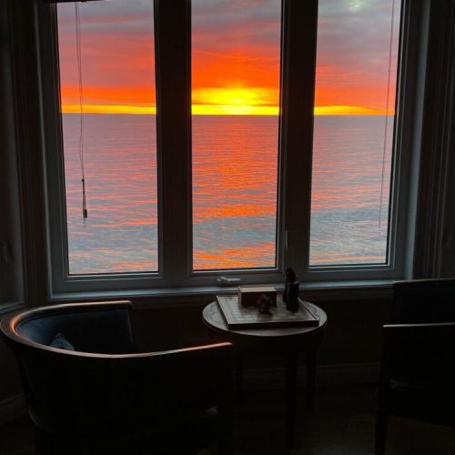 Certainly! Here's a short and professional description for the photo:

---

A stunning sunset view over calm waters, framed by large bay windows in a cozy seating area. Warm light fills the room, creating a serene and inviting atmosphere.