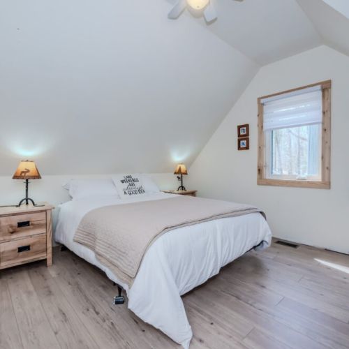 Bright and airy main bedroom featuring forest views, cozy bedding, and a ceiling fan — an ideal retreat for a relaxing cottage vacation stay.