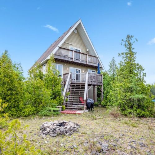 The back of the cottage opens to a spacious lower area, firepit, and wooded pathways—made for outdoor enjoyment.