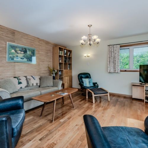 Bright and welcoming living space with rustic touches, comfy seating, and large windows bringing in the forest views of Howdenvale.