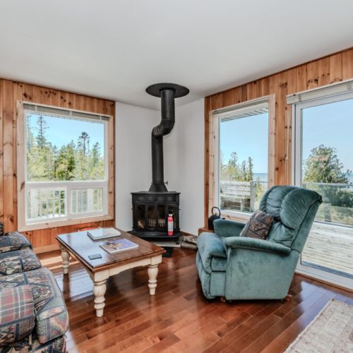 Living room with wood stove and expansive water views — unwind and soak in the natural beauty from the comfort of your cozy cottage.