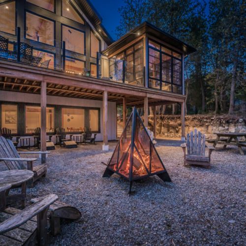 Gather around the fire pit at this stunning vacation rental featuring expansive glass windows, multiple lounge areas, and a forest backdrop—perfect for cozy nights, group getaways, or tranquil nature escapes.