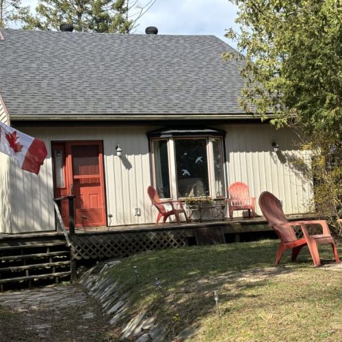 Patriotic Porch: The Canadian flag flies proudly at The Louise, reflecting the heritage and spirit of the locale. The porch, with its red door and comfortable seating, serves as a promise of the hospitality and peaceful relaxation that guests can expect during their stay.