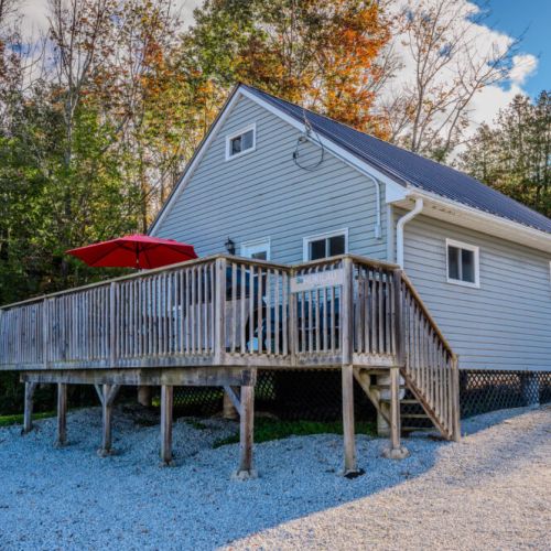 The Hukilau cabin features an elevated deck surrounded by lush trees, offering a peaceful and scenic retreat.